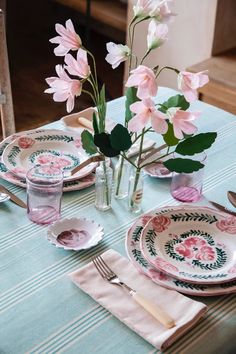 a table set with pink flowers in vases, plates and utensils on it