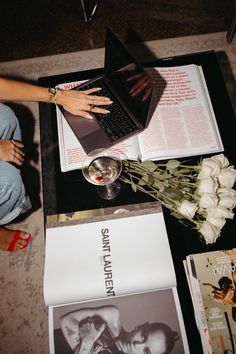 a woman sitting at a table with a laptop and flowers on top of the table