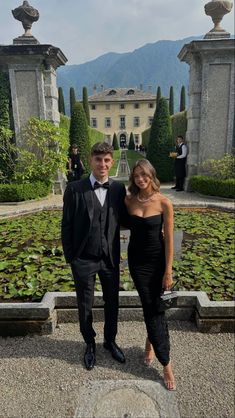 two people in formal wear standing next to each other near some water lilies and trees