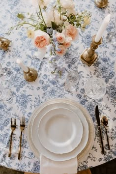 the table is set with white plates and silverware, gold candlesticks, and pink flowers