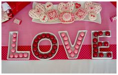 the word love spelled out with candy and candies in front of it on a pink table cloth