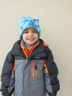 a young boy wearing a blue and gray jacket with an orange hood on his head