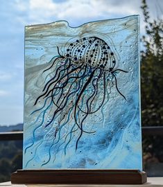 an art glass piece with a jellyfish on it's face and blue water in the background