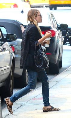 a woman walking down the street with her hand in her pocket and holding a coffee cup