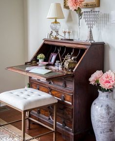 a desk with a chair, vase and flowers on it