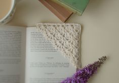 an open book with crocheted triangle next to a purple flower