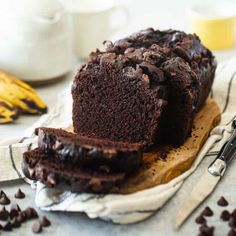 a loaf of chocolate cake sitting on top of a wooden cutting board next to bananas