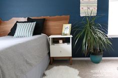 a bed room with a neatly made bed and a potted plant next to it