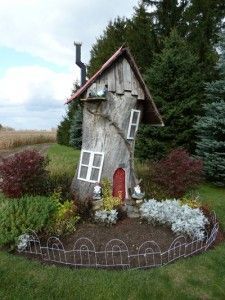 a house made out of a tree stump in the middle of a yard with flowers around it