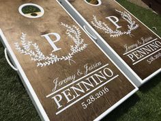 two cornhole game boards with the names and date printed on them sitting in grass