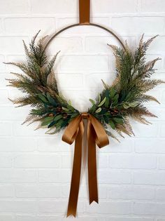 a wreath hanging on a brick wall with a brown ribbon around it and some greenery