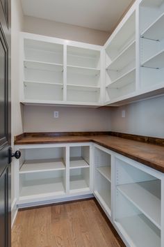 an empty pantry with white shelves and wood flooring on the side walk in closet