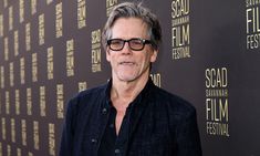 an older man wearing glasses standing in front of a black wall with gold lettering on it