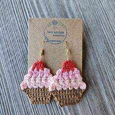 a pair of crocheted earrings on top of a piece of cardboard sitting on a wooden table