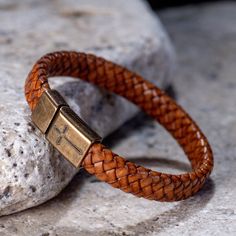 a brown leather bracelet with a gold plated clasp on it sitting on top of a rock