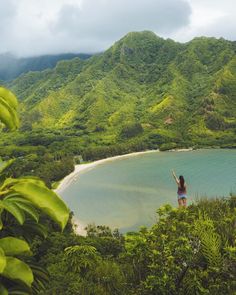 a woman standing on top of a lush green hillside next to a body of water