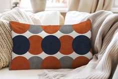 an orange and blue pillow sitting on top of a white couch next to a window