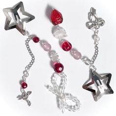 three star charms are hanging from chains on a white surface, one is red and the other is silver