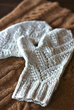 two white knitted mittens laying on top of a brown blanket next to each other