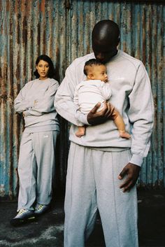 a man holding a baby while standing next to two women in front of a corrugated wall