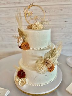 a three tiered white wedding cake with flowers and feathers on the top, sitting on a table