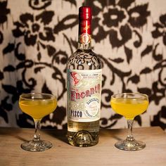 a bottle of booze next to two goblets filled with orange juice on a wooden table