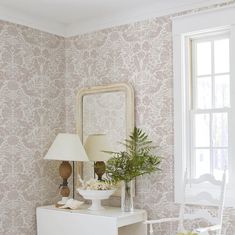 a white table with a lamp and mirror on it in front of a wallpapered room