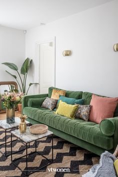 a living room with green couches and colorful pillows on the sofa, coffee table