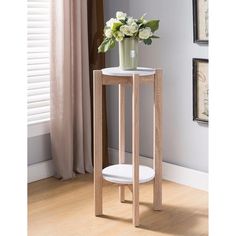 a white vase with flowers sitting on top of a wooden table next to a window