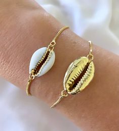 Features genuine Cowrie Shells, dipped in gold plating and affixed to a 14k gold filled box style chain. The bracelet is fully adjustable for a customized fit. Simply slide the gripper disc to your liking. It holds securely. Choose from White with gold trim or All gold. (Bamboo Cuff bracelet shown layered is available separately in the shop) Makes a great gift! I have Cowrie Necklaces available in the shop as well, so take a look around! *Please avoid showering, swimming or spraying perfume with Dainty Gold Bracelets For Beach, Dainty Gold Beach Bracelets, Dainty Gold Bracelet For Beach, Resizable Gold Jewelry As A Gift, Trendy Adjustable Gold-tone Jewelry, Adjustable Gold Plated Jewelry For Gift, Adjustable Gold-plated Jewelry For Gifts, Dainty White Resizable Jewelry, Gold Friendship Bracelets With Adjustable Length