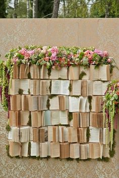 a wall made out of books with flowers growing on them and moss growing over the pages