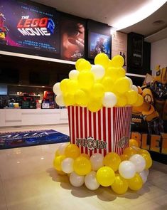 a popcorn box filled with yellow and white balloons sitting on top of a counter next to a movie poster