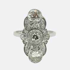 Here we have a truly beautiful Art Deco diamond ring. The ring features three vertically set old cut diamonds the largest of which is approximately 1.0 carat and sits in the centre. The face of the ring also features a further 16 smaller old cut diamonds and is finished with elegant milgrain detail. It dates back to the 1920s and is just as stylish today as it would have been 100 years ago. Condition: Used (Very Good) Weight: 5.8 grams Size: L (52) Face Dimensions: 24mm x 13mm Central Diamond: A Antique Oval Three Stone Diamond Ring, Antique Three Stone Diamond Ring In Diamond White, Art Deco Three Stone Diamond White Ring, Diamond White Three Stone Art Deco Ring, Vintage White Three Stone Diamond Ring, Heirloom Diamond White Three Stone Diamond Ring, Heirloom Diamond White Diamond Ring With Three Stones, Heirloom Diamond White Ring With Three Stones, Heirloom Three Stone Diamond White Diamond Ring