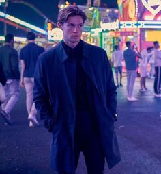 a man standing in the middle of an amusement park at night with people walking around