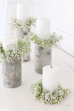 some white candles are sitting in vases with flowers and baby's breath on them