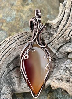 a wire wrapped pendant with a large brown stone in the center on a piece of wood