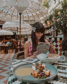 a woman sitting at a table with an open book in front of her and eating food