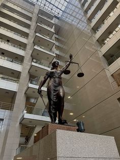 a statue of lady justice in front of a high rise building with glass windows and balconies