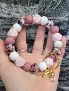 a hand holding a bracelet with pink, white and gold beads on it's wrist