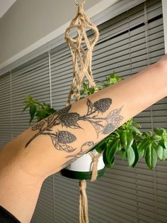 a woman's arm with tattoos on it hanging from a window sill next to a potted plant