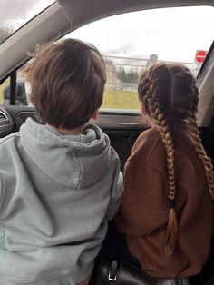 two children sitting in the back seat of a car looking out the window at an open field