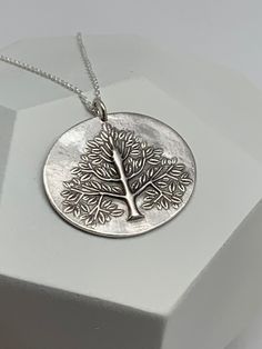 This unique tree of life handmade embossed oval round pendant has been entirely handmade using .999 fine silver. It has been cut from fine silver precious metal clay, textured, fired and oxidized. The pendant hangs from a sterling silver diamond cut cable chain. This fine silver pendant features an embossed tree of life on one side of the pendant and is reversible to a wood grain embossed pattern on the reverse side. Pendant size: approximately 1 x 1 1/4 inches Chain length: adjustable at 16 and Nature-inspired Stamped Jewelry For Everyday, Stamped Oval Pendant Jewelry Gift, Etched Sterling Silver Round Disc Jewelry, Silver Hammered Oval Pendant Jewelry, Oval Pendant Jewelry For Gifts, Everyday Silver Nature-inspired Jewelry, Nature-inspired Stamped Sterling Silver Jewelry, Silver Etched Nature-inspired Necklaces, Nature-inspired Sterling Silver Etched Jewelry