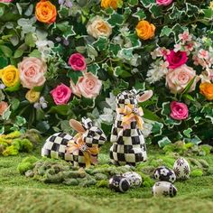 two rabbits sitting in the grass next to some eggs and flowers with pink roses behind them