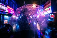 a person standing under an umbrella on a city street at night with neon signs in the background