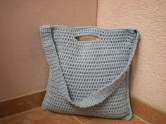 a blue crocheted bag sitting on the floor next to a pink wall with a hole in it