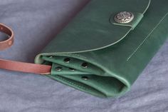 a green leather purse sitting on top of a blue sheet next to a brown strap