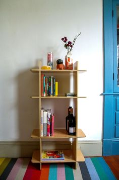 a wooden shelf with books and bottles on it in front of a blue door next to a multicolored rug