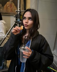 a woman holding a drink in her right hand and looking at the camera while standing next to stairs