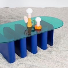 a glass table with three different colored vases sitting on it's sides in the sand