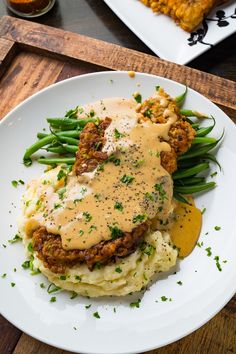 a white plate topped with mashed potatoes covered in gravy and green beans